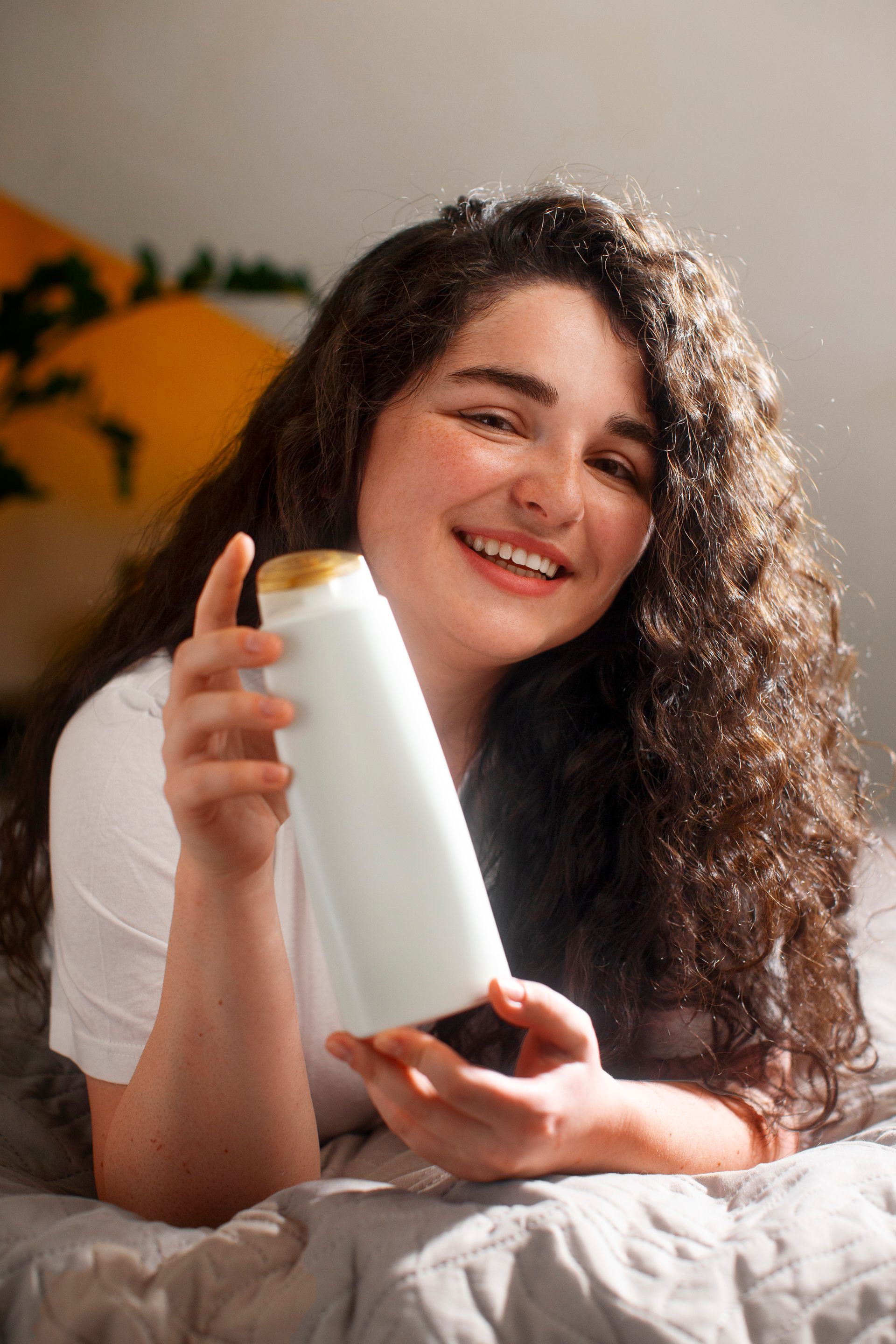 A woman is sitting on a bed holding a bottle of shampoo.