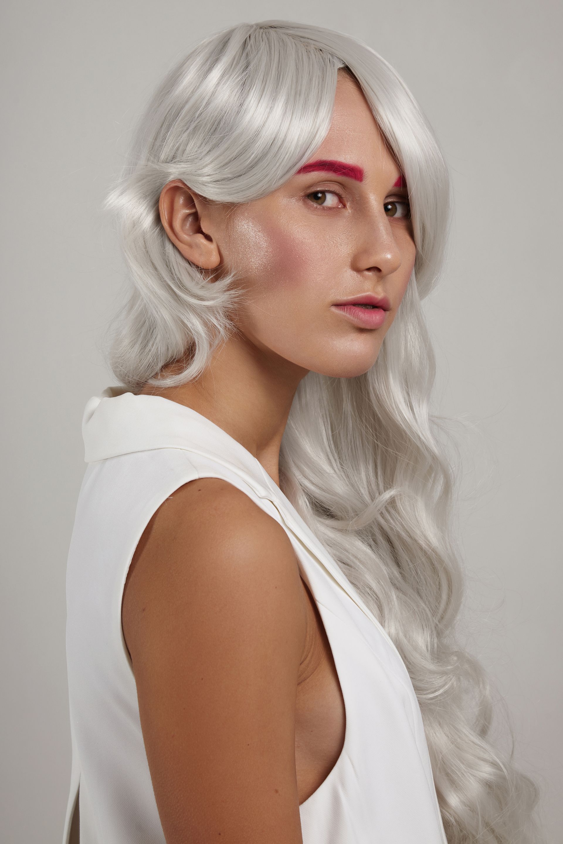 A woman with long white hair and red eyebrows is wearing a white wig.