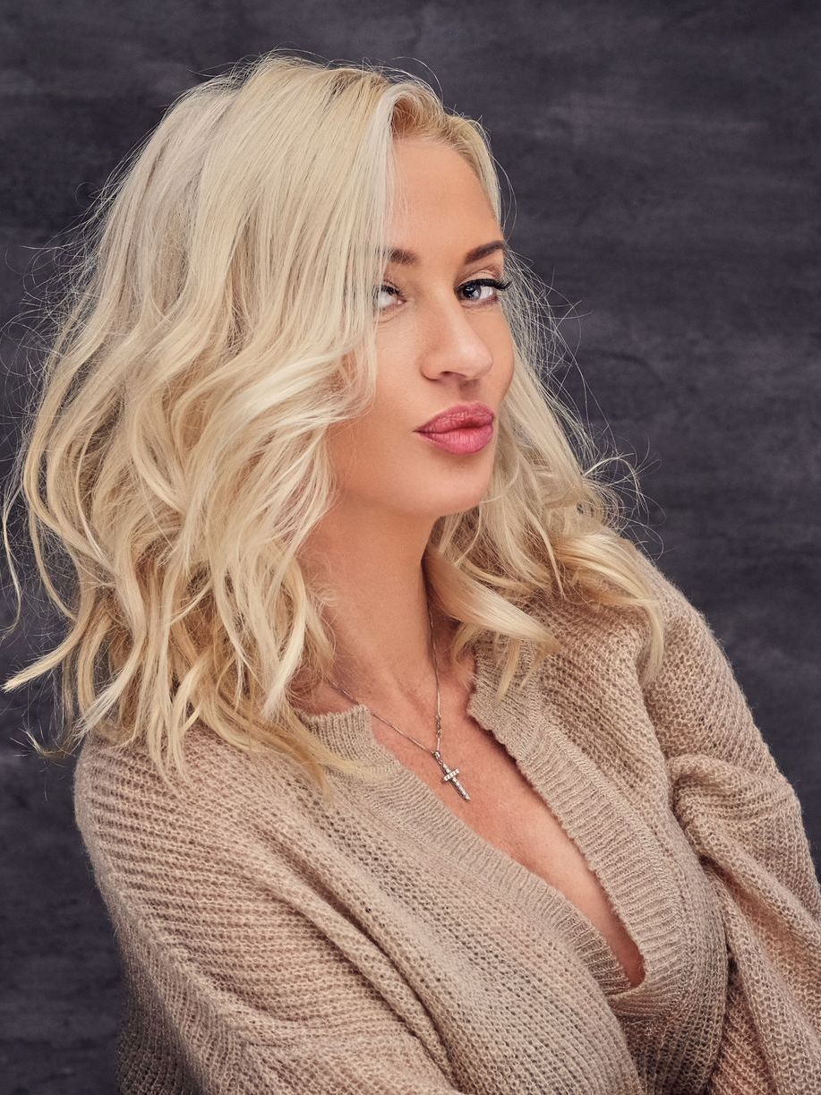 A woman with blonde hair is wearing a sweater and a necklace.