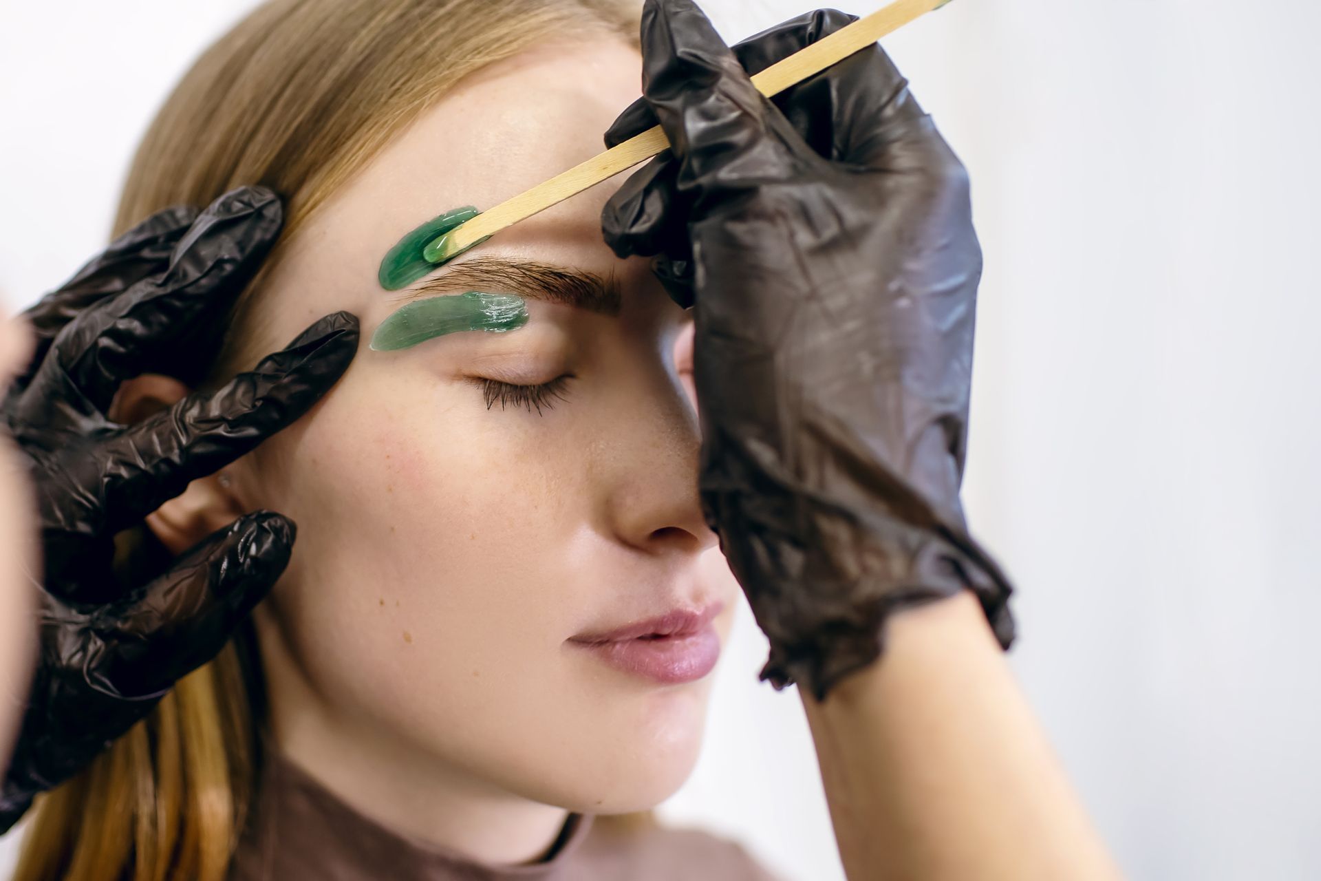 A woman is getting her eyebrows painted by a makeup artist.