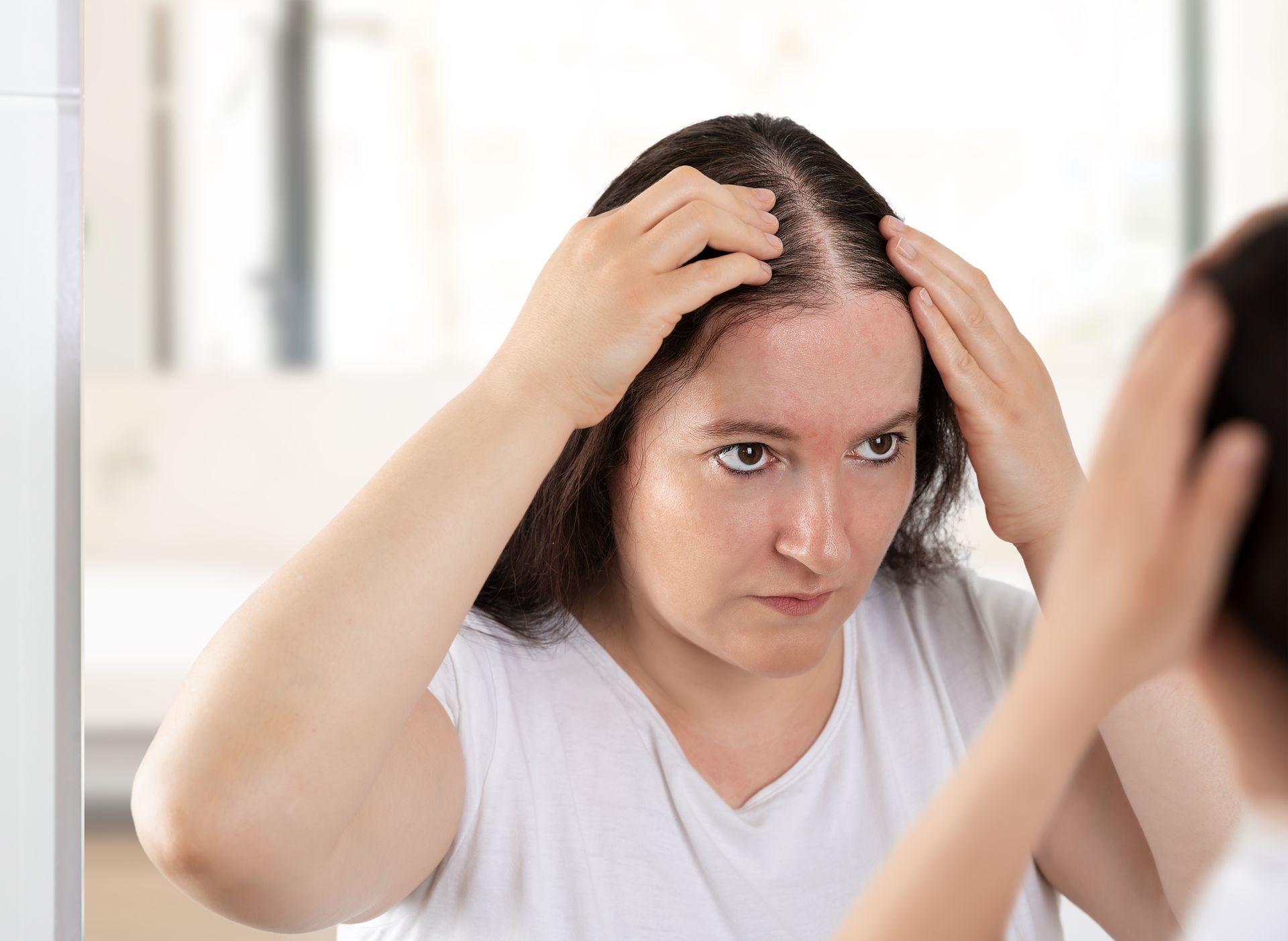 Person checking thinning hair in a bathroom mirror
