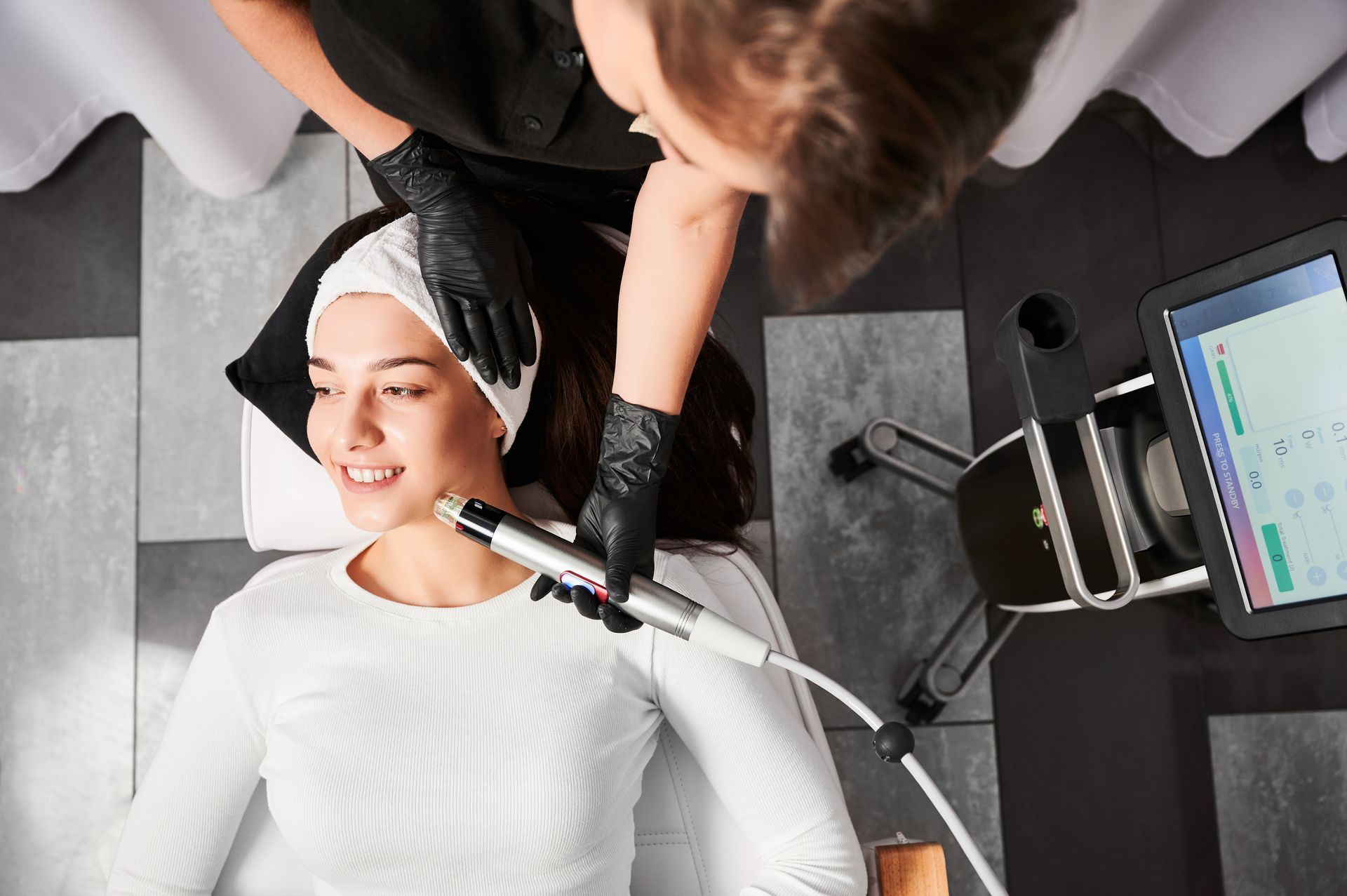 Woman receiving a facial treatment in a spa, lying under a white towel with a technician at her side.