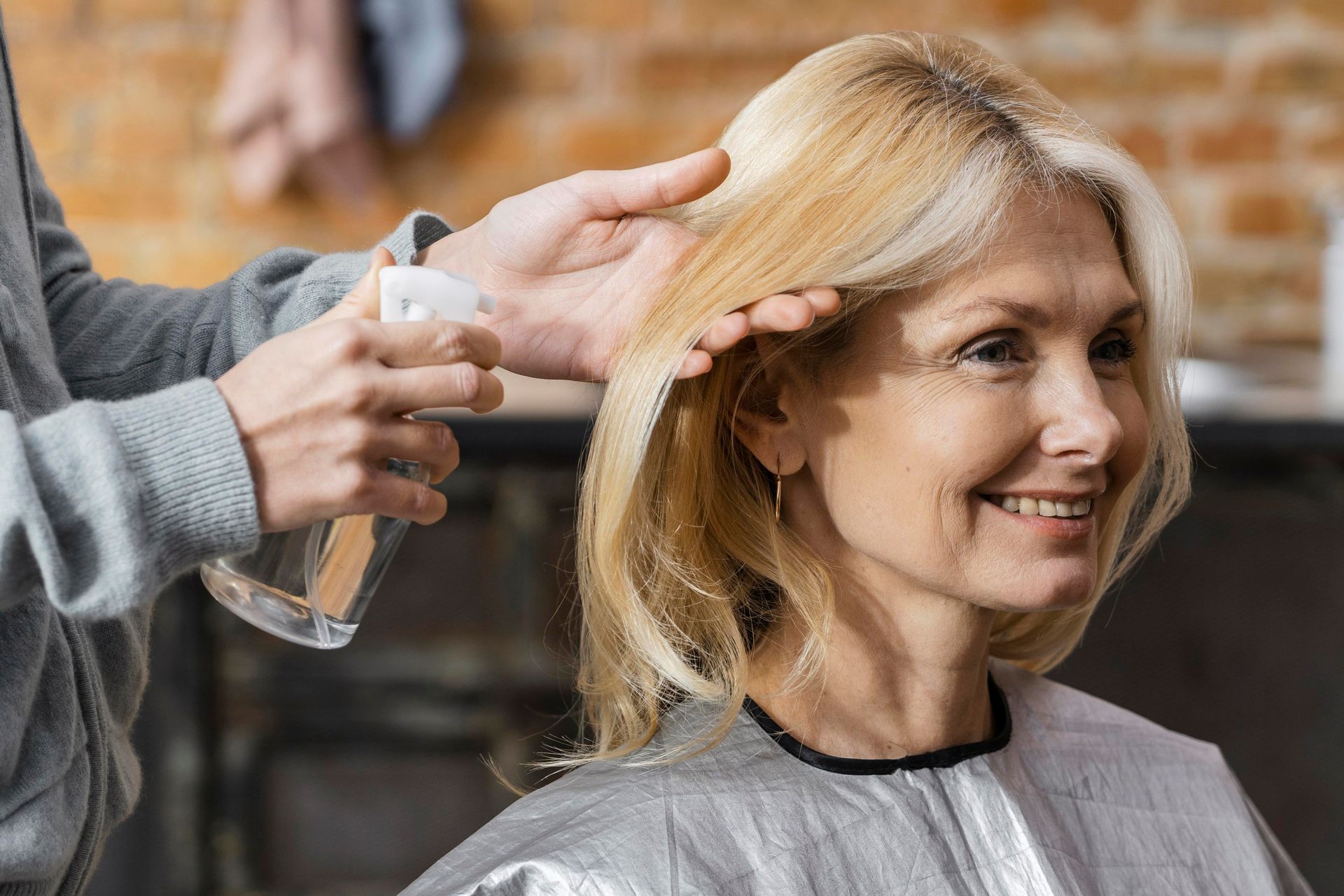 A hairdresser uses a spray bottle on a person's blonde hair in a salon.