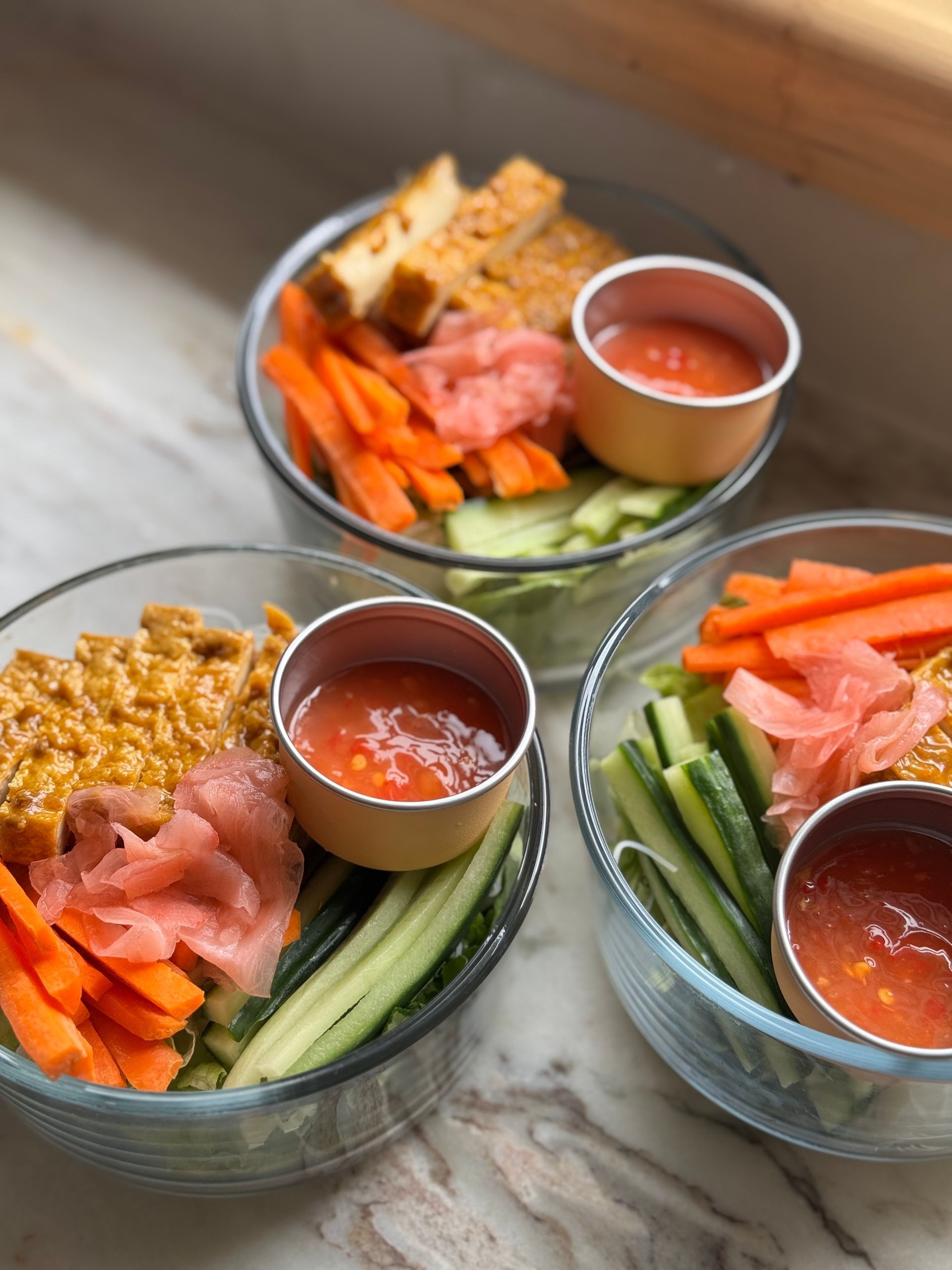 Three bowls of food with sauces and vegetables on a table.
