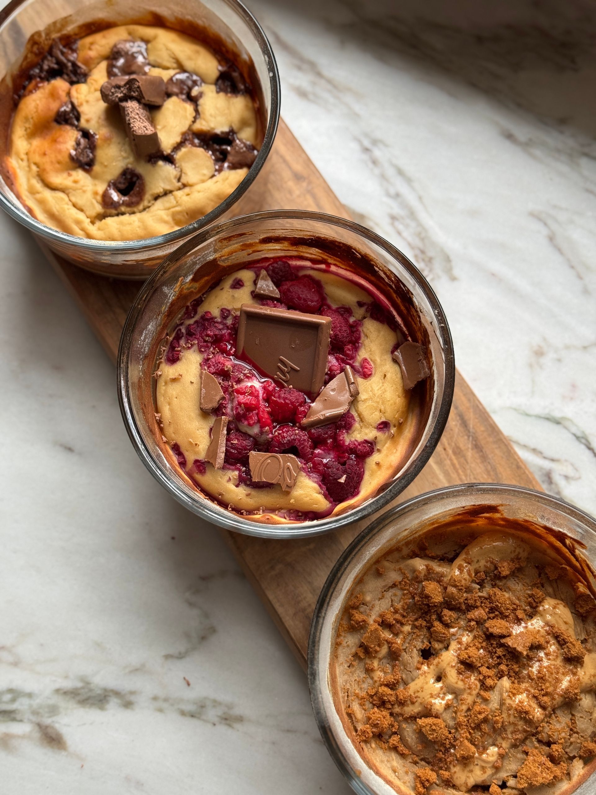 Three desserts are sitting on a wooden cutting board.