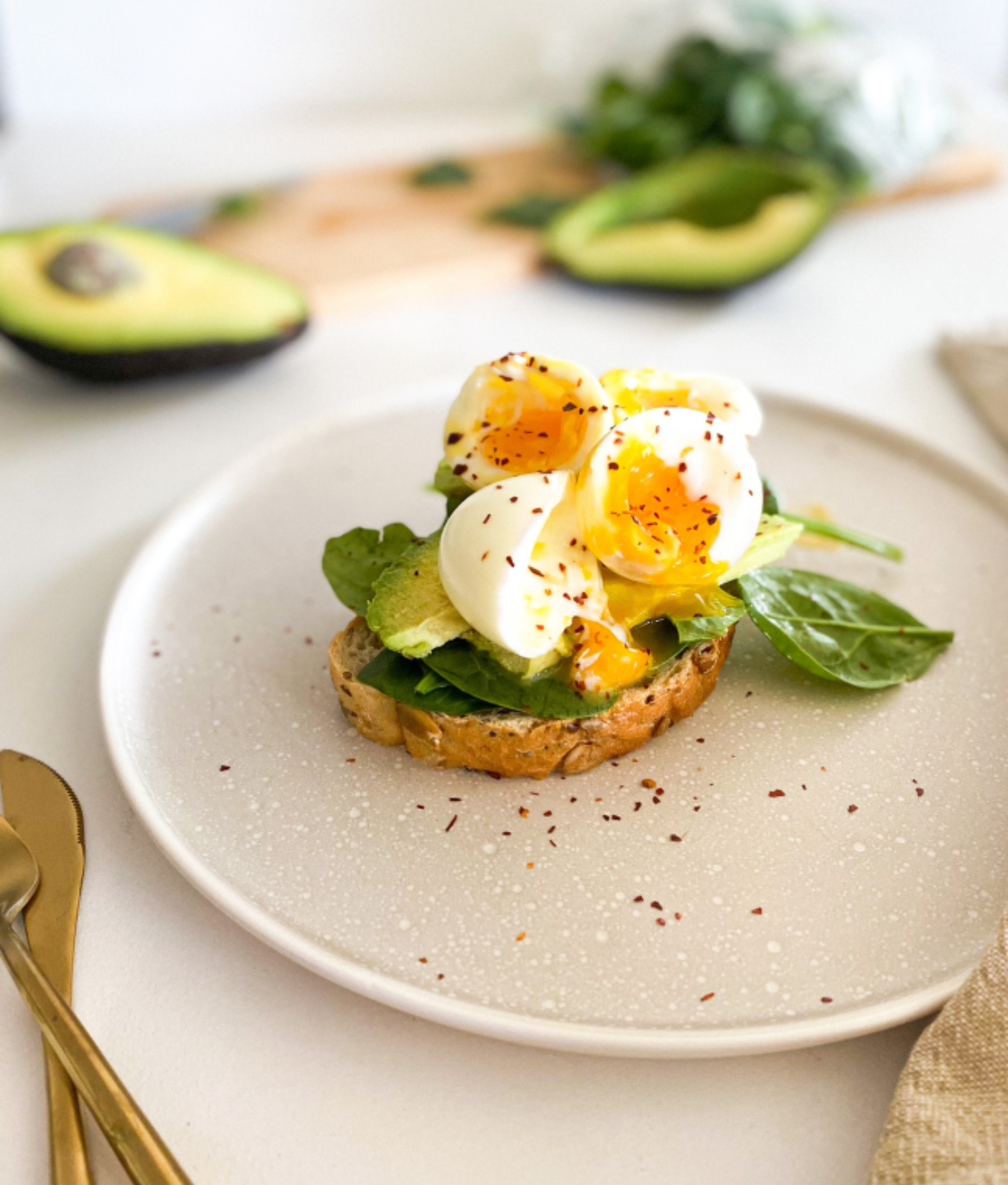 A white plate topped with a sandwich with avocado , spinach and hard boiled eggs.