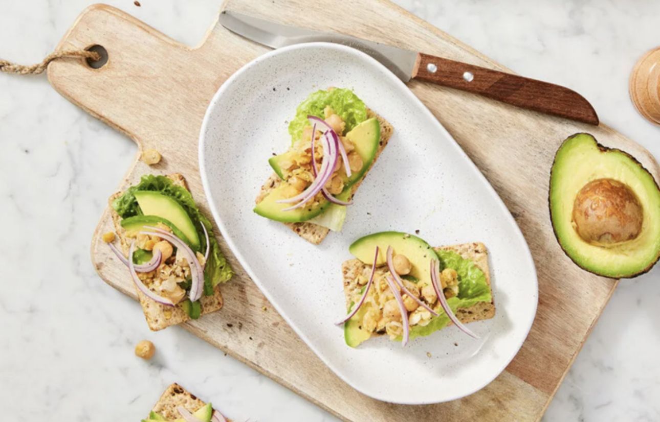 A white plate topped with avocado , chickpeas and onions on a wooden cutting board.