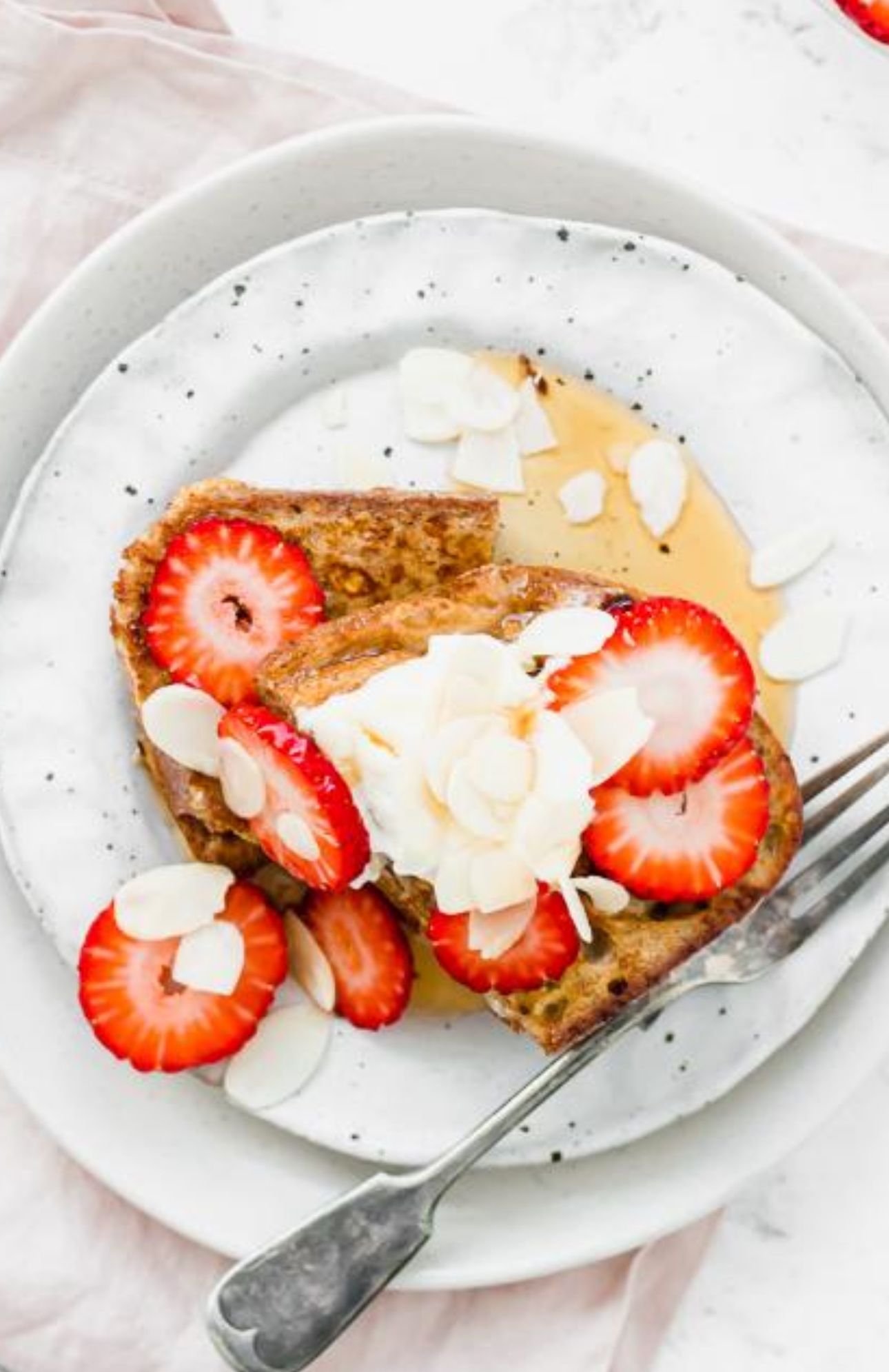 French toast with berries and whipped cream on a black plate with a fork.