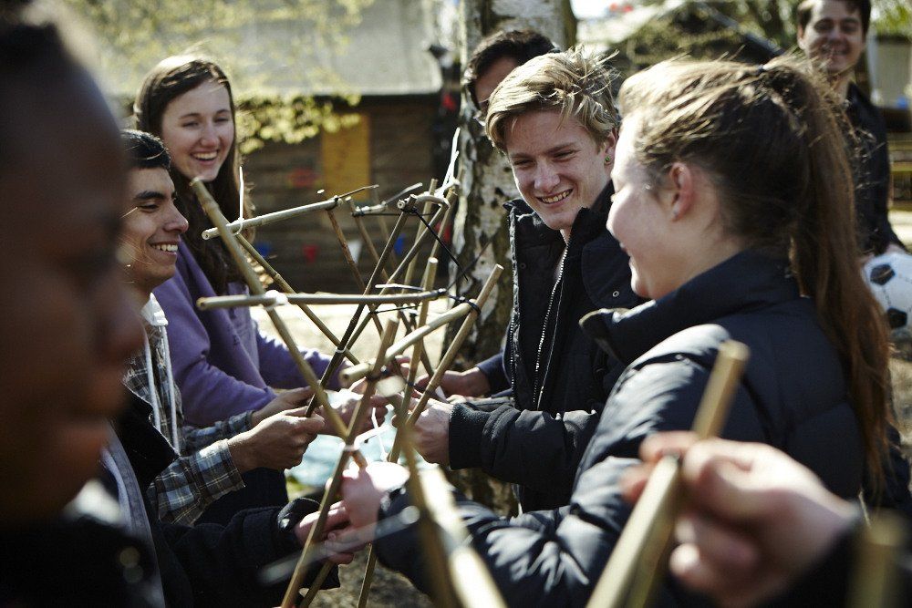 A group of young people are sitting around a table holding sticks.