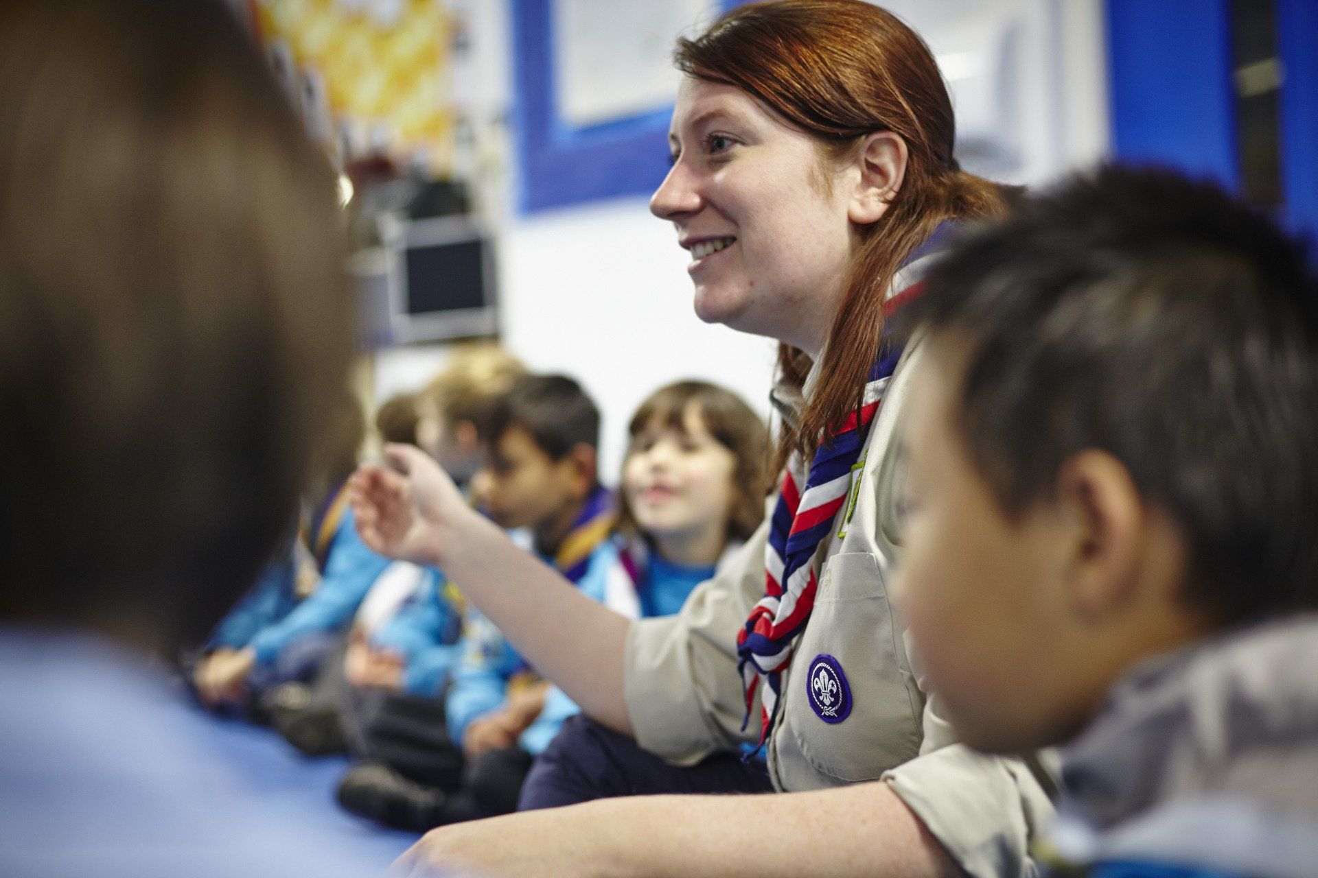 A woman in a scout uniform is talking to a group of children.
