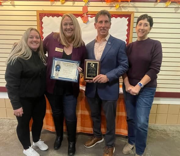 Four people stand indoors holding framed awards in front of a decorated wall.