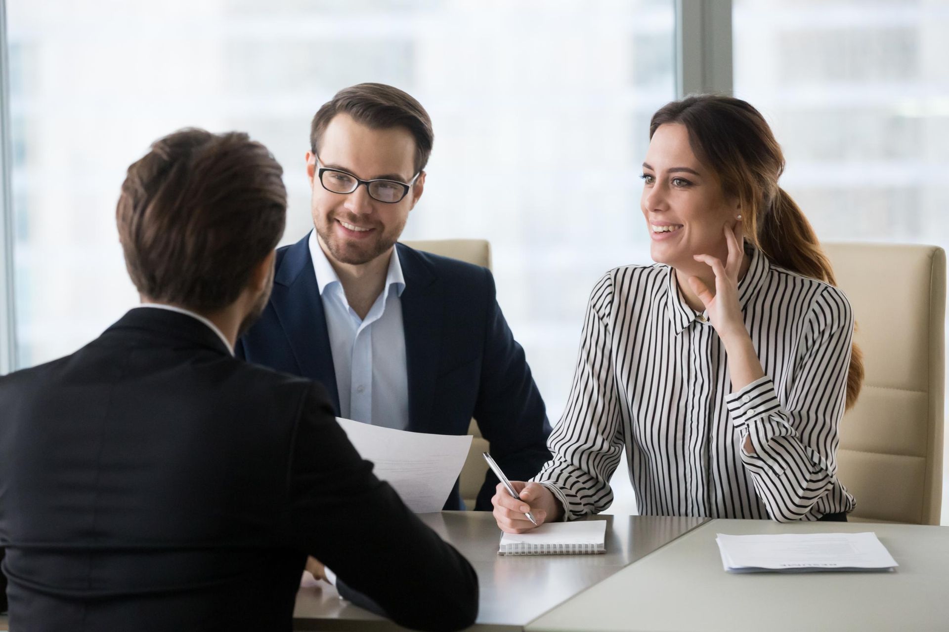 Three people in business attire at a table, discussing documents. Smiling faces, modern office setting.