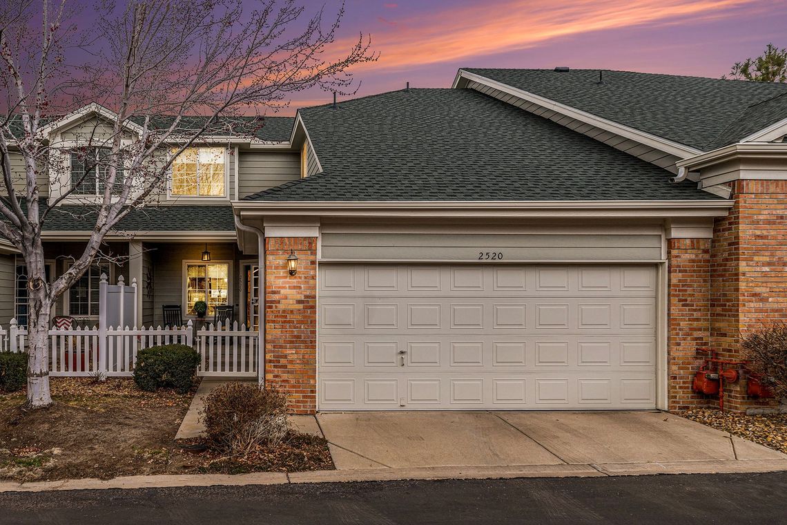 Townhouse exterior with a garage and porch under a colorful sunset.