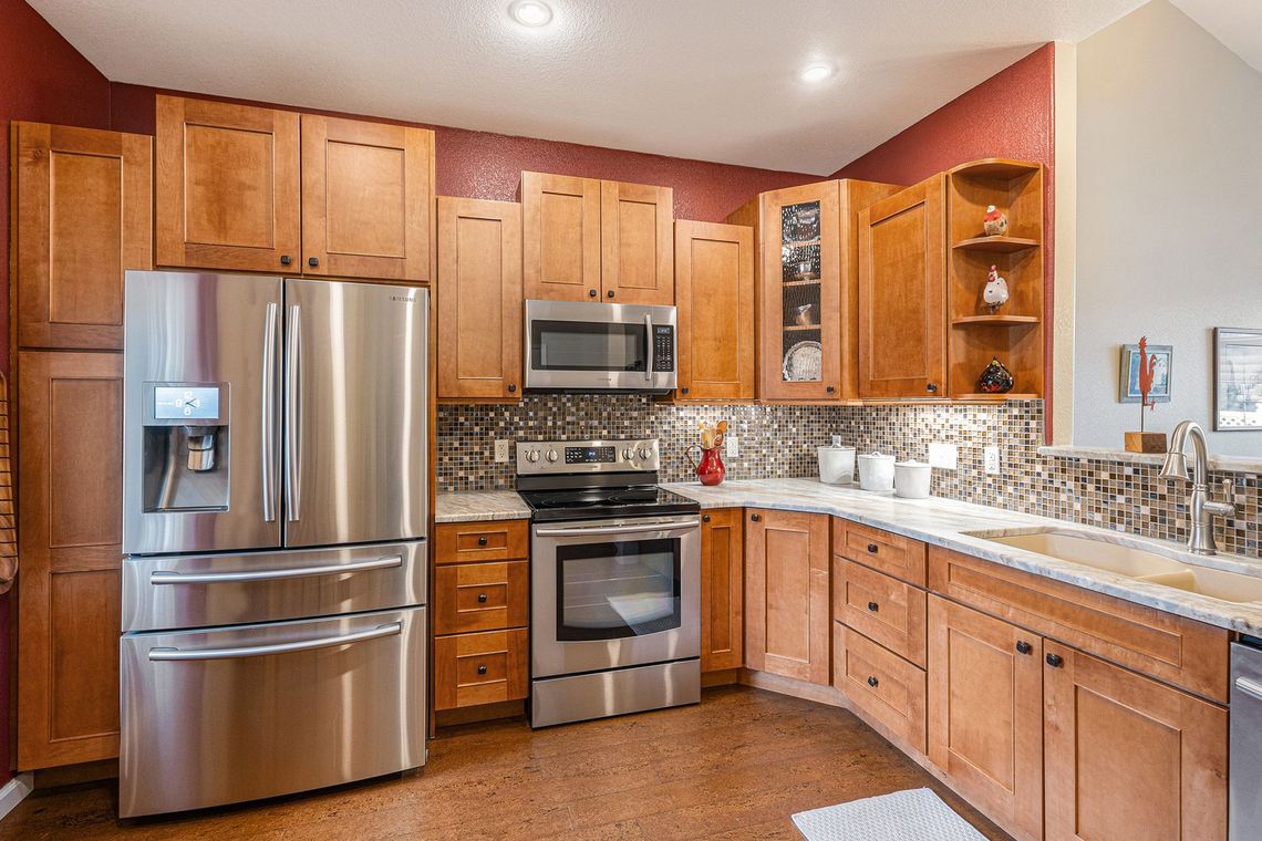 A modern kitchen with stainless steel appliances, wooden cabinets, and a speckled backsplash.