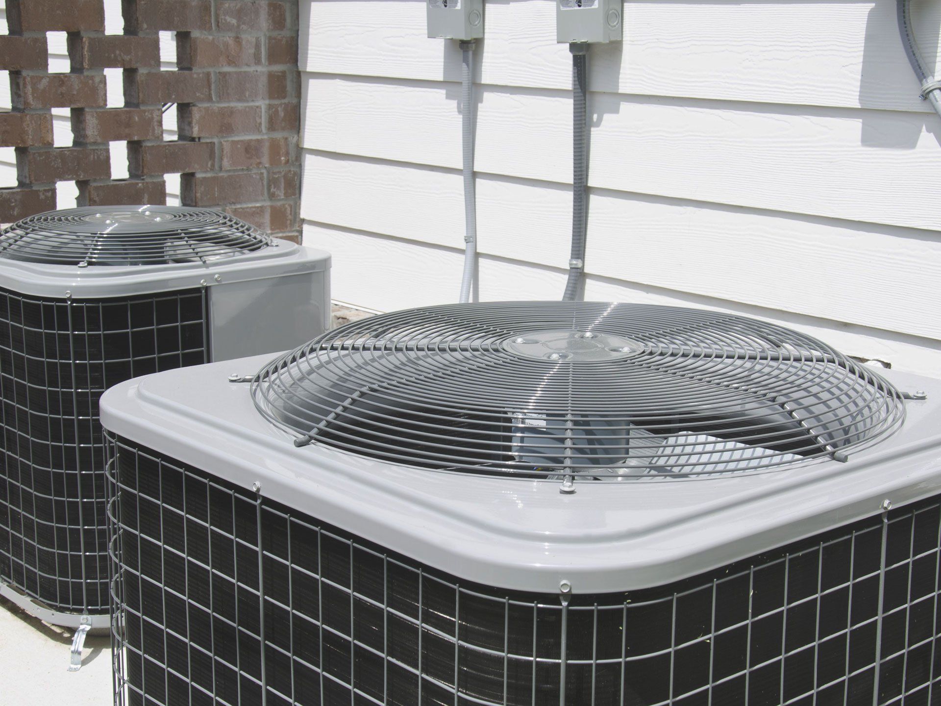 Two outdoor air conditioning units beside a house wall