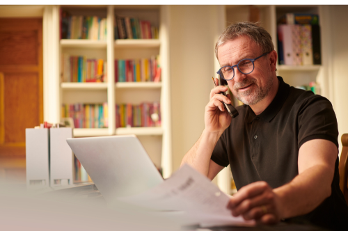 Man in glasses on a phone call at a laptop in a home office with bookshelves