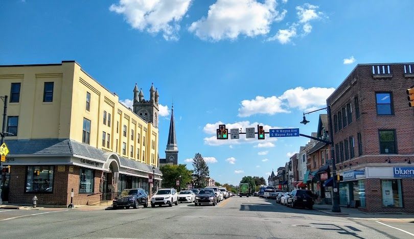 Downtown street intersection with cars, storefronts, and traffic lights under a blue sky