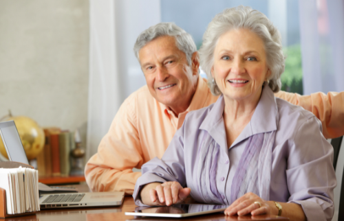 Smiling couple sitting at a table with a laptop and tablet in a bright home setting
