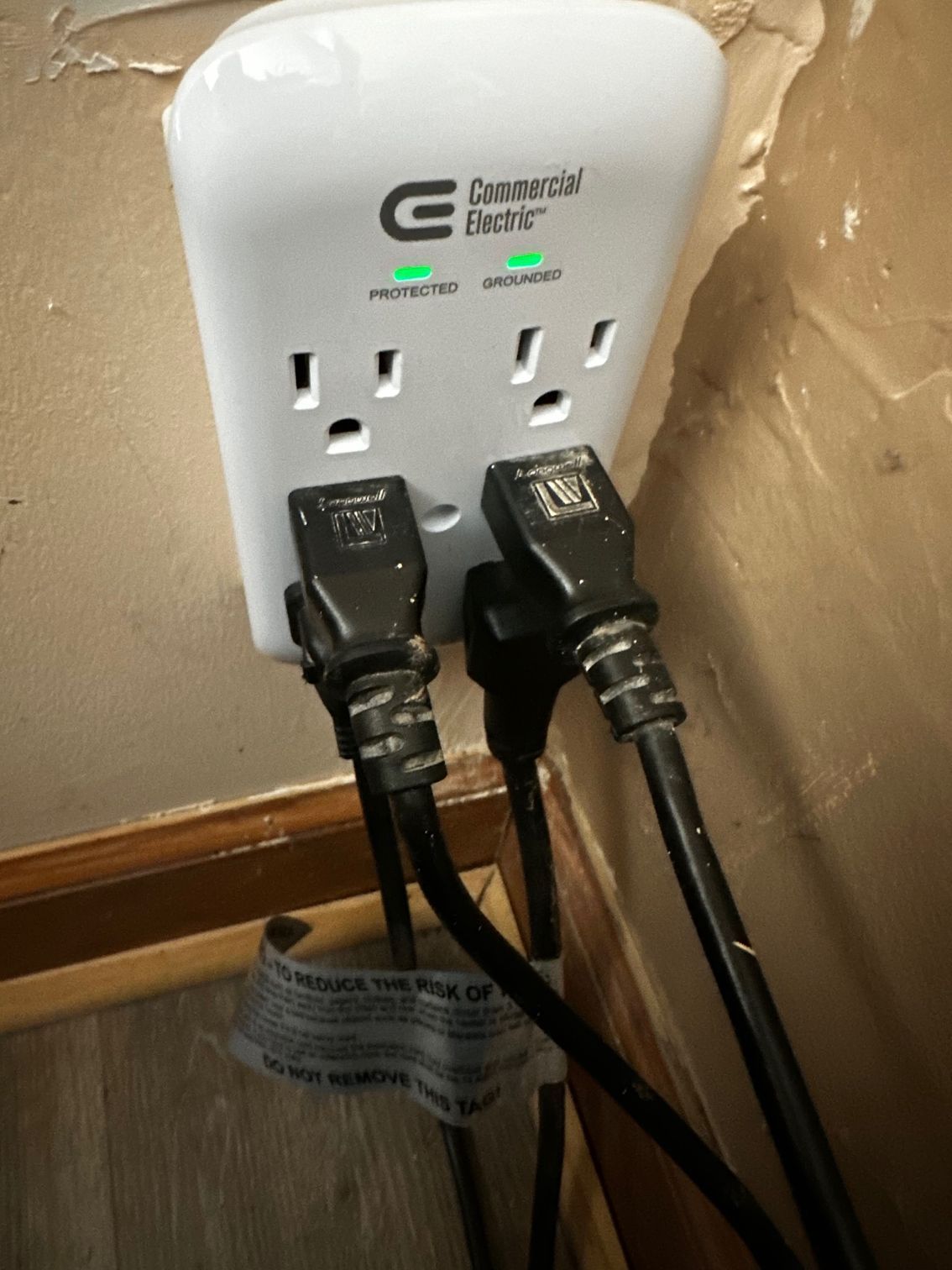 Two black plugs in a white wall outlet with green indicator lights on a surge protector.