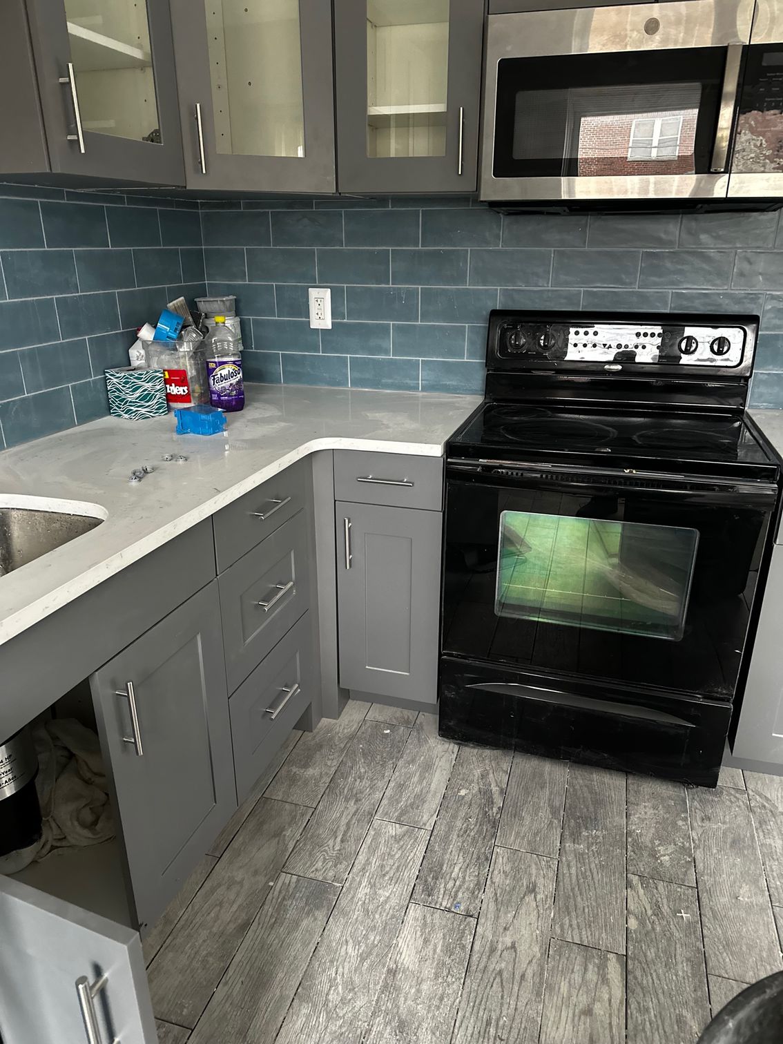 Modern kitchen with gray cabinets, white countertops, blue tile backsplash, and a black stove and microwave.