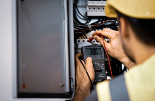 Electrician testing wiring in an open electrical panel with a multimeter.