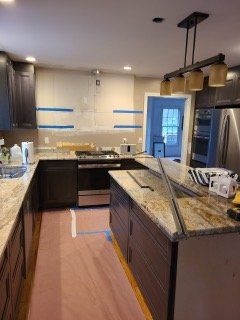 Modern kitchen with granite island, dark cabinets, stainless appliances, and blue painter’s tape on the walls.