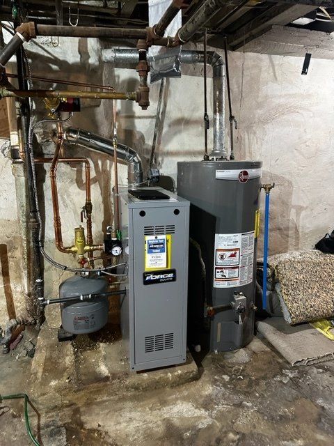 Basement utility area with two gray furnaces, exposed pipes, and a water heater against unfinished walls