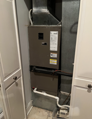Residential HVAC furnace in a closet with exposed ducts and pipes