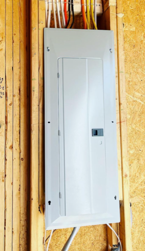 White electrical breaker panel mounted on unfinished wood wall in a construction area