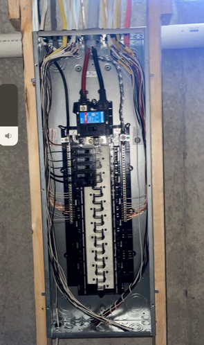 Open electrical breaker panel with wiring and blue digital display inside a wall recess