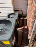 Outdoor air conditioner units in a narrow side yard beside a brick wall and house siding