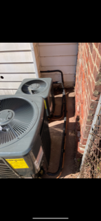 Outdoor air conditioner units beside a brick wall and house siding in a narrow side yard