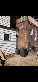 Side of a house with white siding and red brick, two black trash bins, and a small dirt yard.