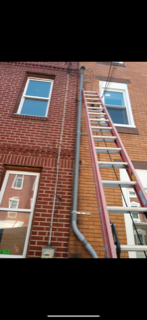 Ladders leaning against a red brick building beside windows and drainpipes.