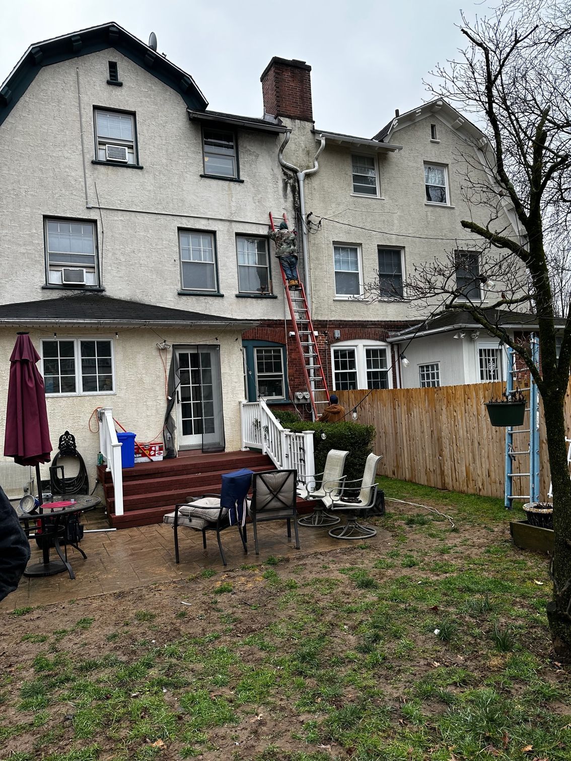Backyard of a row house with patio chairs, table, umbrella, and a wooden fence under overcast skies