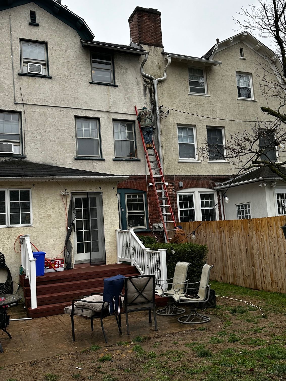 Backyard of a townhouse with a red ladder against the upper wall and outdoor furniture on a patio.
