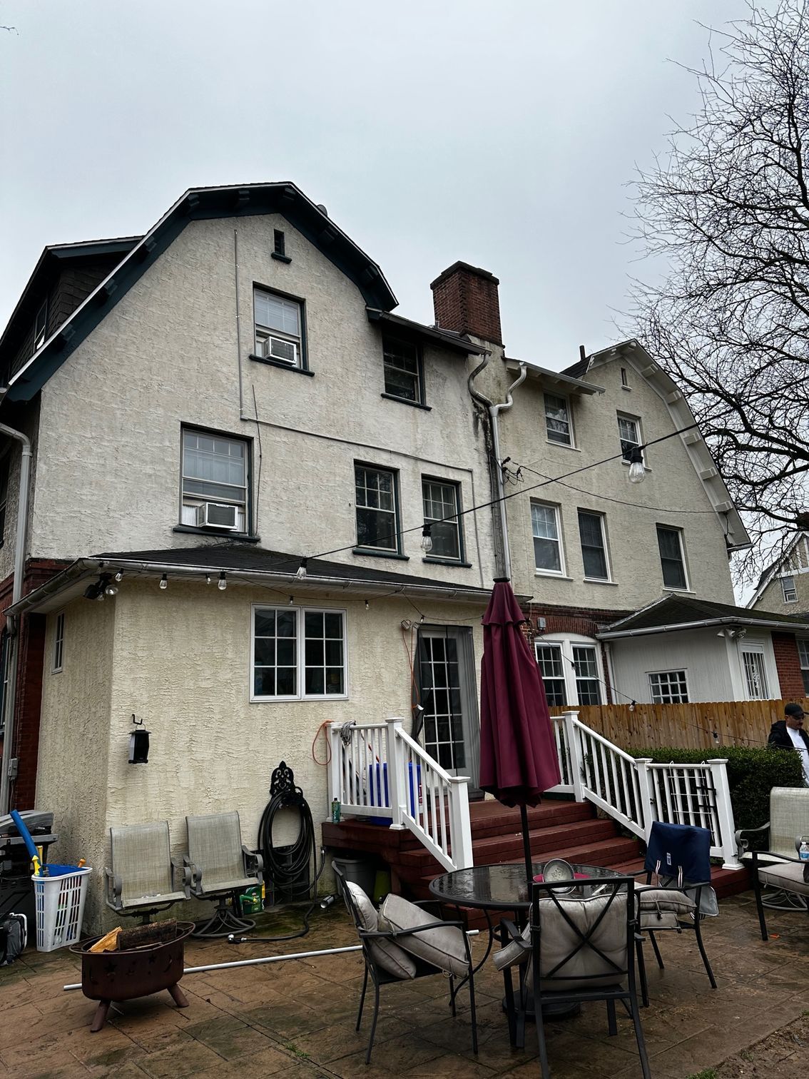 Multi-story white house with patio furniture and a red umbrella in a rainy backyard
