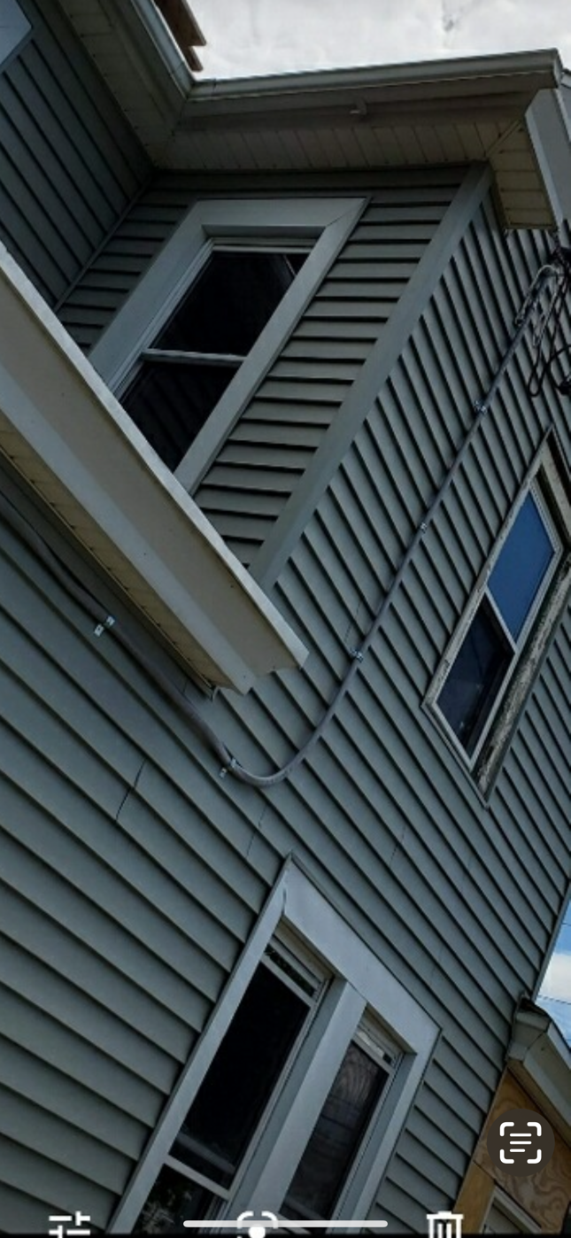 Tilted view of a gray house exterior with white-trimmed windows and beige roof eaves