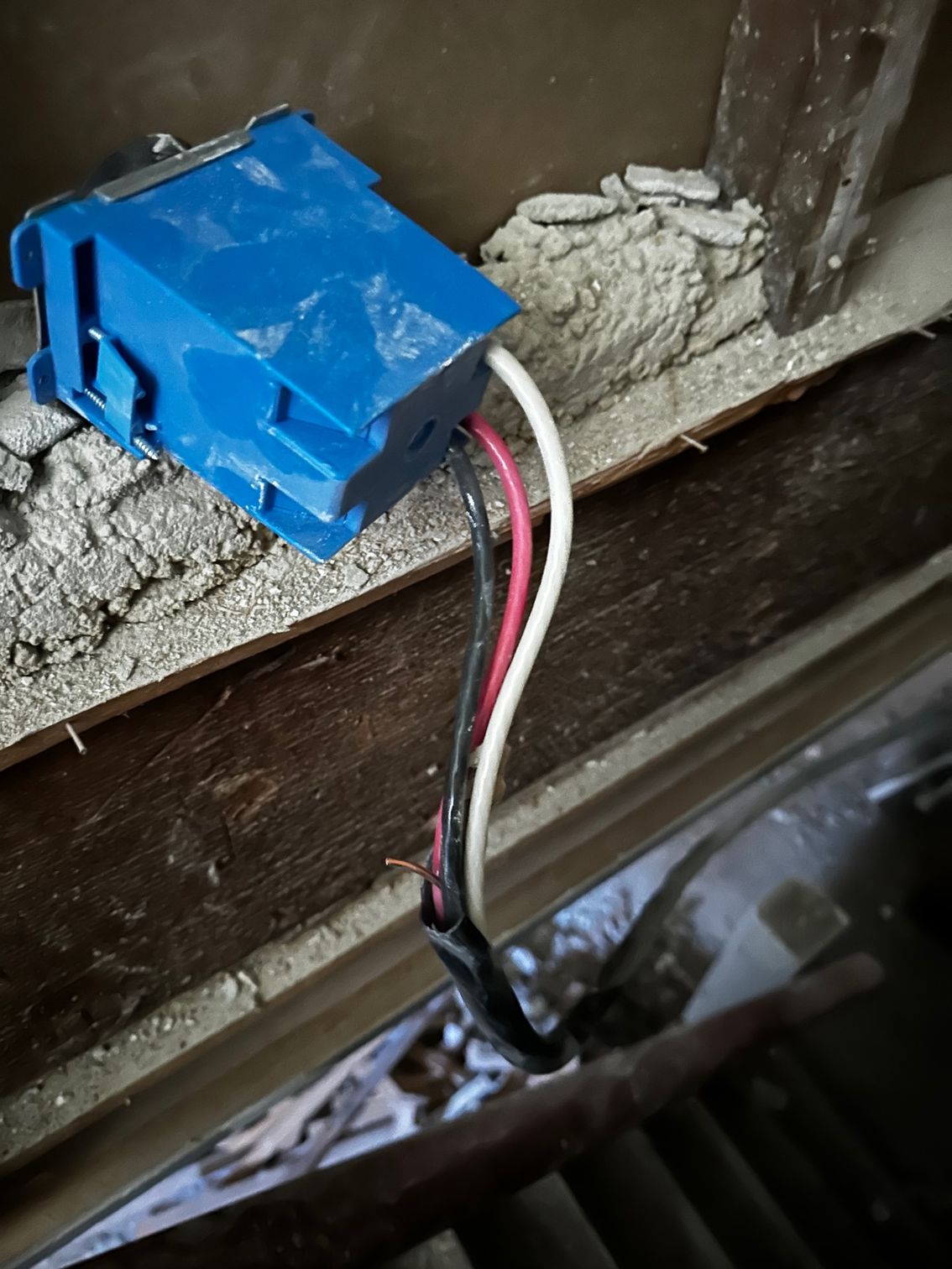 Blue electrical connector with red, white, and black wires inside a dusty wooden opening