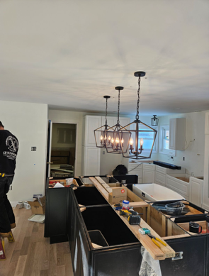 Kitchen under renovation with island, sink, chandelier, and worker near doorway