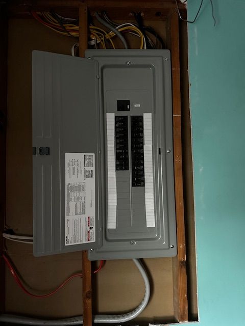 Open electrical breaker panel with multiple switches in a wall cavity, door ajar.