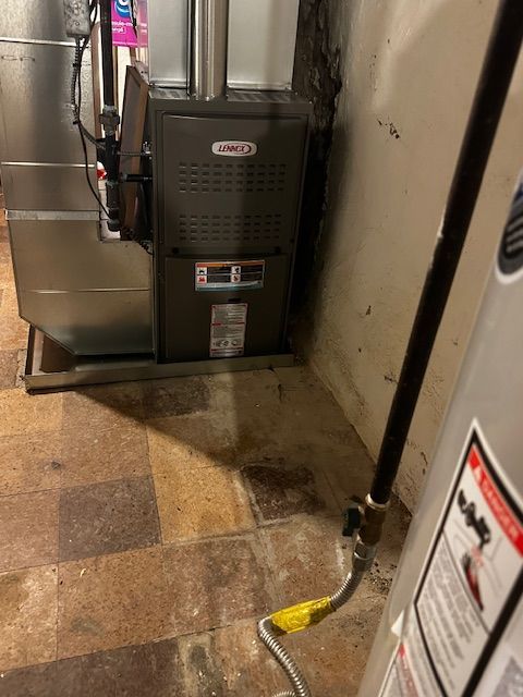 Furnace unit in a narrow basement hallway with a yellow cord on the floor and water stains nearby