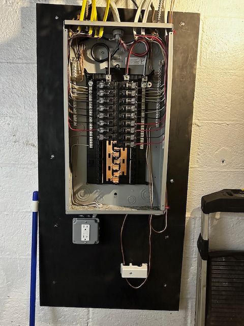 Open electrical breaker panel with wiring and switches mounted on a black board.