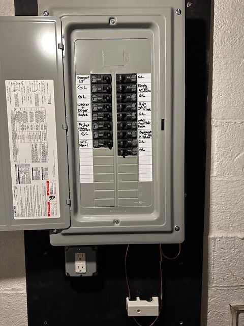 Open electrical breaker panel with labeled switches and cover door in a utility room.
