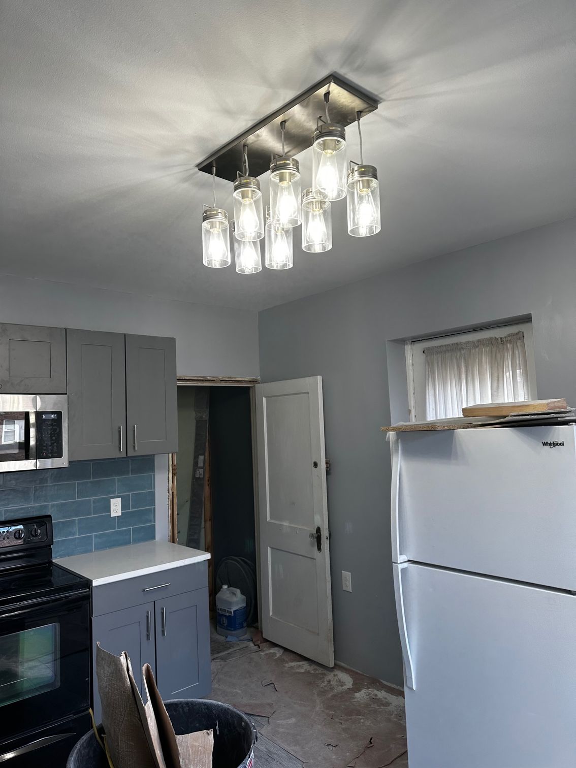 Small kitchen with gray cabinets, blue tile backsplash, white fridge, and modern ceiling light fixture.