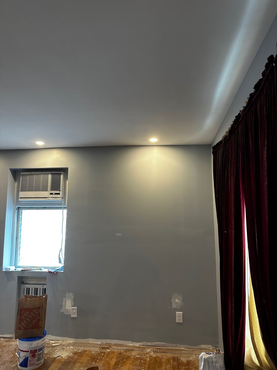 Empty gray room with a small window, recessed ceiling light, and dark curtains.