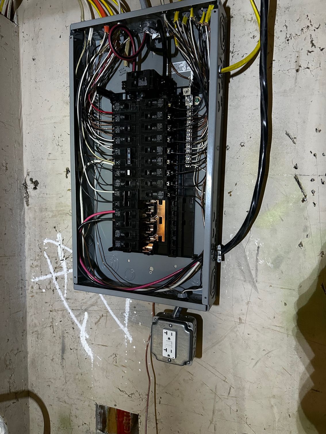 Open electrical breaker panel with exposed wiring mounted on a wall near a small box below.