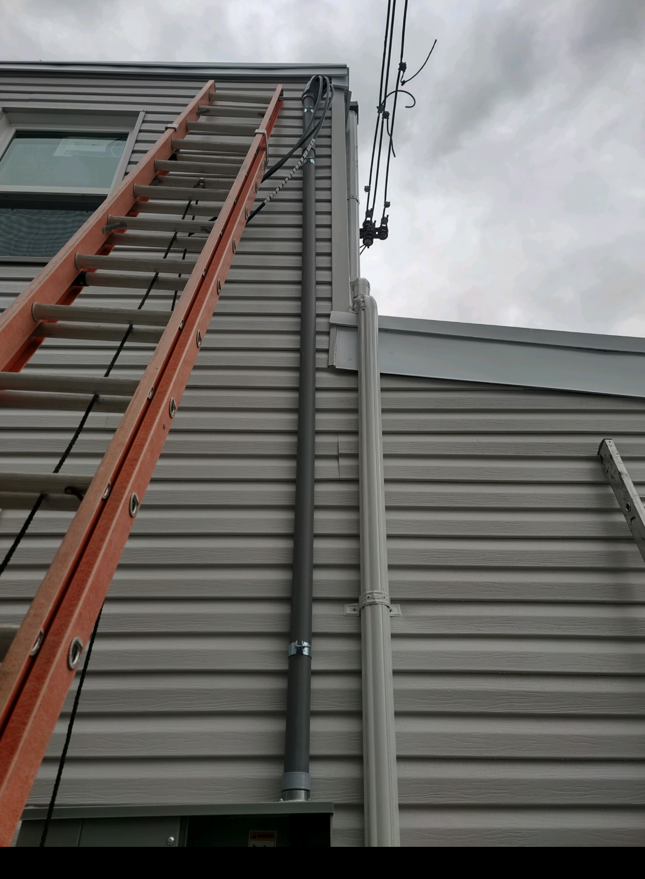 Orange ladder leaning against gray building siding and roof edge under cloudy sky