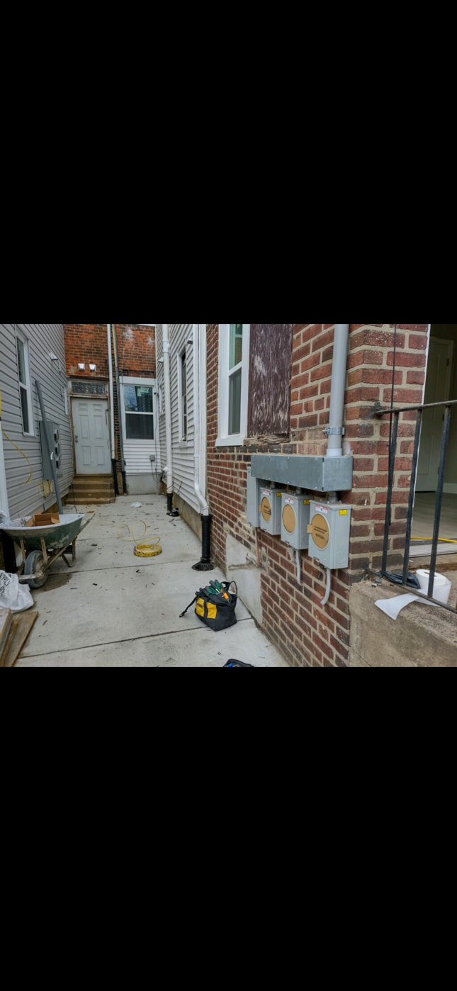Narrow brick-lined alley with outdoor utility meters, bins, and scattered leaves on the ground