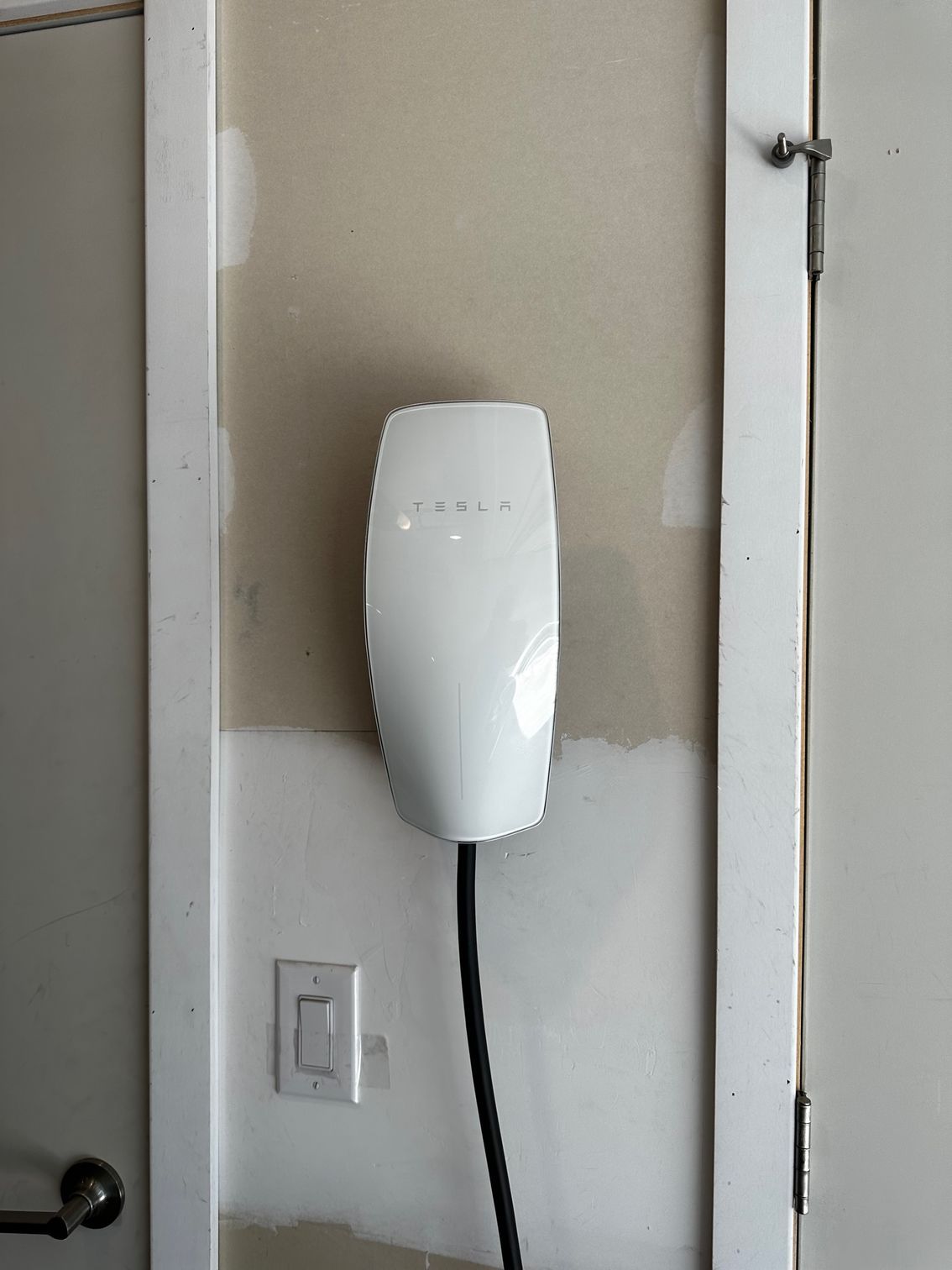 White wall-mounted device with black cord beside a light switch on a beige wall